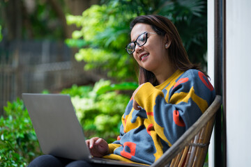 A young Asian woman wearing a yellow floral-pattern sweater and sunglasses, smiling brightly while...