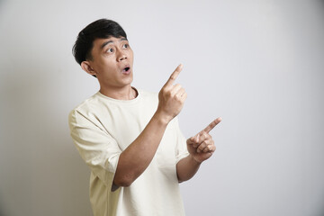 A surprised Asian man looks up with his mouth open in shock, while pointing with both index...