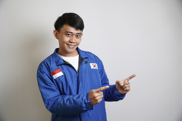 A man in a blue jacket smiles and points to the side, against a plain white background.