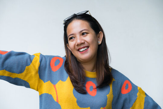 Young Asian woman in colorful sweater smiling while standing in front of a white wall, casual portrait concept.
- Powered by Adobe