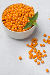 Bowl filled with sea buckthorn berries with mint leaf on grey background, close up. Healthy eating, vitamins concept.