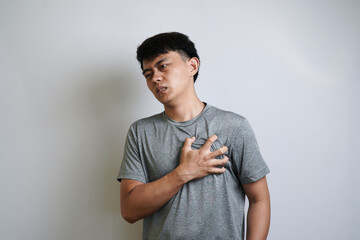 A young Asian man holds his chest with a pained expression and grimaces, showing symptoms of heart problems or chest pain.