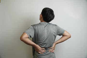 A young Asian man seen from behind, showing that he is suffering from back pain, holding his lower...