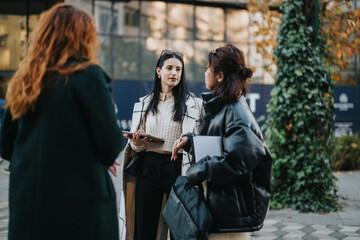 Three women engage in discussion outside, surrounded by urban settings and greenery, fostering...