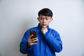 Pensive young Asian man in a blue uniform deeply engrossed in thought while intently viewing...