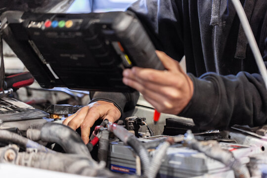 Aussie workman using digital diagnostics tool working on car vehicle engine in mechanics workshop