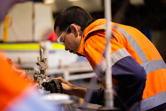 Young male mechanic in high-vis working on a complex car engine problem inside industrial workshop
