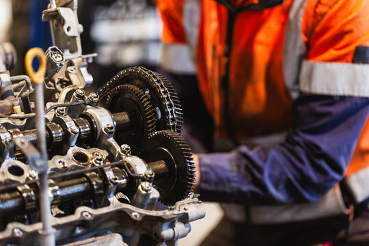 Male mechanic working on a car engine repair inside industrial workshop focus on machinery
