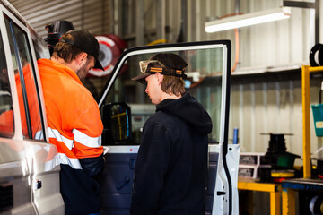 Aussie mechanics standing at open drivers side door of a vehicle inside industrial workshop