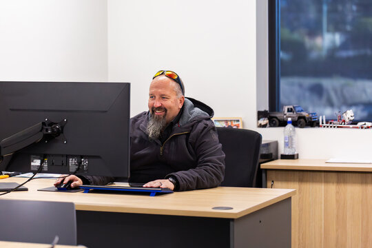 Business owner seated at desk in office indoors smiling at computer screen