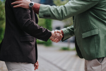 Close-up of two individuals engaged in a handshake while outdoors, emphasizing professionalism,...