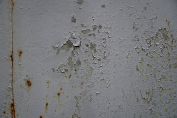 A detailed close-up reveals a heavily weathered metal surface, showcasing extensive peeling light grey paint and prominent patches of orange rust.
