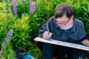 Teen boy with Down syndrome painting on canvas in a lupine meadow inclusive art class and...