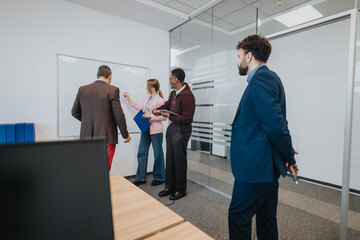 A diverse team of business professionals standing and reviewing data on a whiteboard.