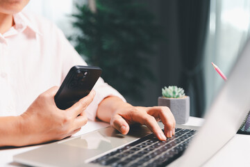 Close-up shot, woman sits at a wooden table using her smartphone, with her finger touching the...