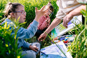 Inclusive outdoor art class: teacher gently guiding two children with Down syndrome as they paint...