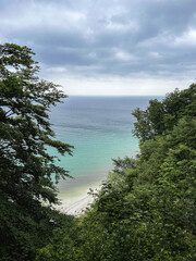 Ocean with small beach and turquoise blue water and cloudy sky between green trees and bushes