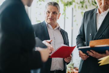 Group of professionals having a productive conversation while reviewing documents in an office setting. The image captures teamwork and collaboration in a corporate environment.