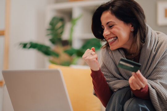 Excited woman celebrating online shopping success with credit card and laptop