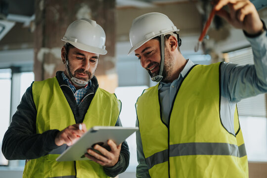 Construction team collaborating on plans using a tablet, wearing safety vests and helmets, symbolizing planning and teamwork in an industrial setting.