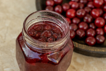 A close-up of a jar filled with delicious homemade cherry jam, accompanied by fresh cherries in the background creating a rustic culinary setting.