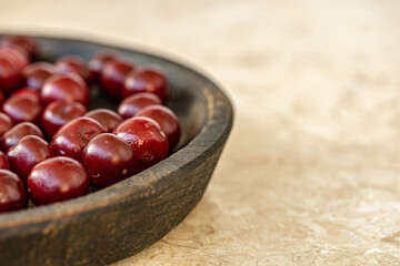 Close up of Fresh Red Cherries in a Rustic Wooden Bowl on Beige Surface with copy space