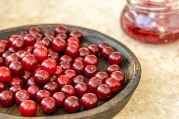 .           Wooden bowl with fresh, ripe red cherries next to a jar of bright red jam in the kitchen. Farm-to-table concept
