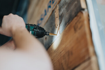 Focused view of a person operating a drill on a wooden plank during a construction or woodworking...