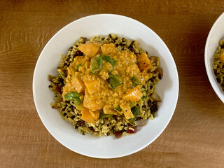 Vegan Sri Lankan sambar curry served on a bed of spicy rice in a white bowl on a wooden tabletop, highlighting plant-based cuisine, aromatic spices, and healthy eating
