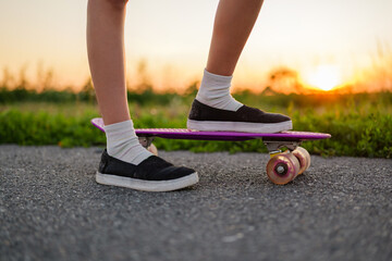A close-up of a person's legs and feet standing on a purple skateboard on an asphalt road during a...
