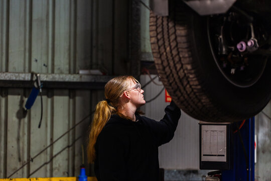 Long-haired female mechanic operating a control panel of blue hydraulic lift system in workshop