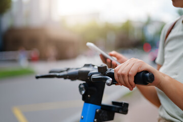 A close-up of a person's hands using a smartphone to unlock or operate an electric scooter on a...