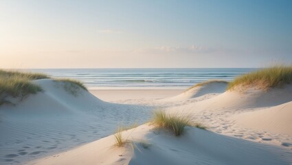 Sunny beach with sand dunes and grassy patches, leading to calm ocean waves under a clear sky.