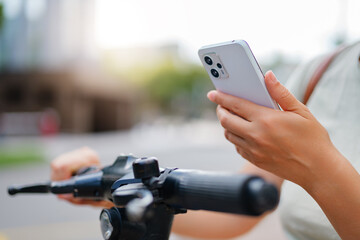 
A close-up shot of a person's hands using a smartphone to operate an electric scooter, highlighting the integration of technology and urban transport.