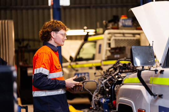 Aussie workman using digital diagnostics tool working on car vehicle engine in mechanics workshop