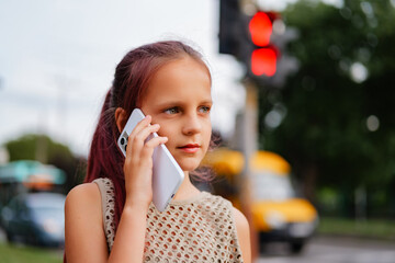 A serious young girl on a city street talks on a smartphone, looking away with a focused expression...