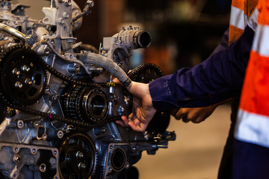 Mechanics hand holding part of vehicles internal engine inside industrial workshop