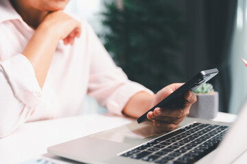 Close-up shot, woman sits at a wooden table using her smartphone, with her finger touching the phone screen as she navigates mobile banking, online shopping, and social media networks.