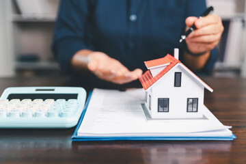 House model placed on table alongside coins, paperwork symbolizes real estate investment, property...