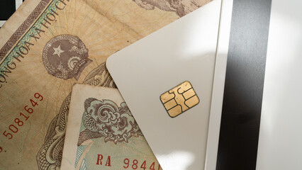 Close up image of white credit card with chip placed top of various banknotes, suggesting themes of finance and currency exchange. composition highlights contrast between modern digital payment