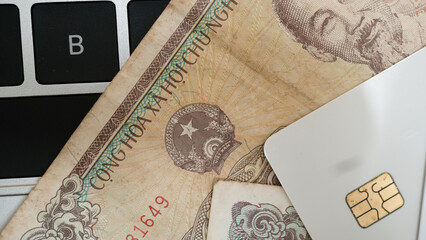Close up image of Vietnamese currency notes partially covering laptop keyboard, with credit card placed on top, suggesting themes of finance and technology