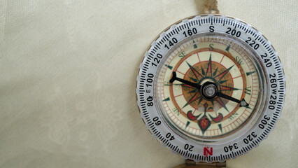 Vintage compass with detailed rose design is shown against textured beige background, highlighting its intricate markings and directional indicators