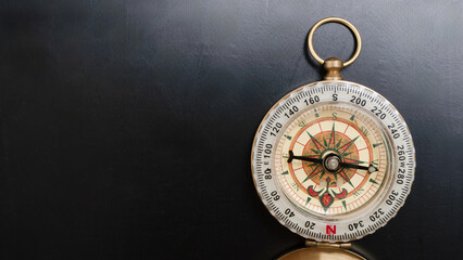 Vintage brass compass with detailed rose design lies on dark surface, evoking sense of exploration and adventure. compass needle points north, symbolizing guidance