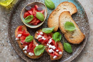 Classic bruschettas with tomatoes, feta cheese and green basil served on a brown plate, horizontal shot, middle close-up