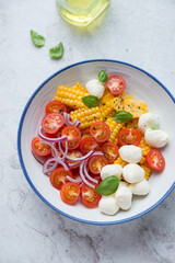 Salad with sweet corn, cherry tomatoes and mini mozzarella, vertical shot on a white stone background, elevated view