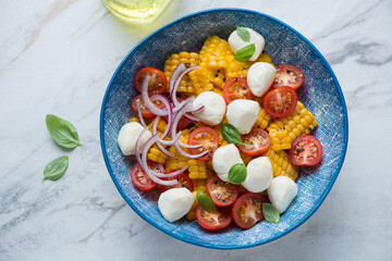 Cherry tomato, mini mozzarella and corn salad served in a blue bowl, horizontal shot on a white granite background, high angle view