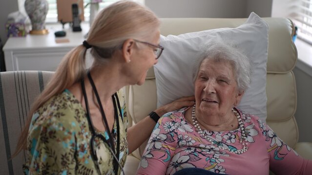 A nurse checks the vitals of an elderly woman during a friendly visit at a senior living facility, engaging in warm conversation and providing support.