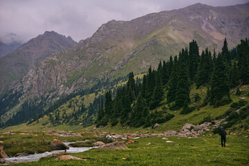A backpacker walks along a mountain path along a river in a mountain valley