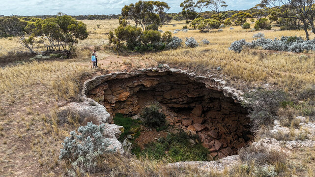 Aerial of two kids looking into a remote sinkhole