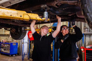 female mechanic tradeswomen working together on car repair in industrial workshop